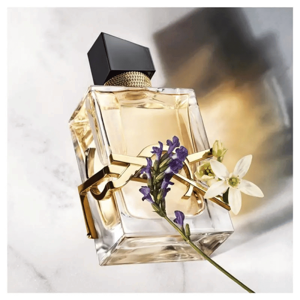 A bottle of Yves Saint Laurent Libre perfume, with a stem of lavender and a white flower.
